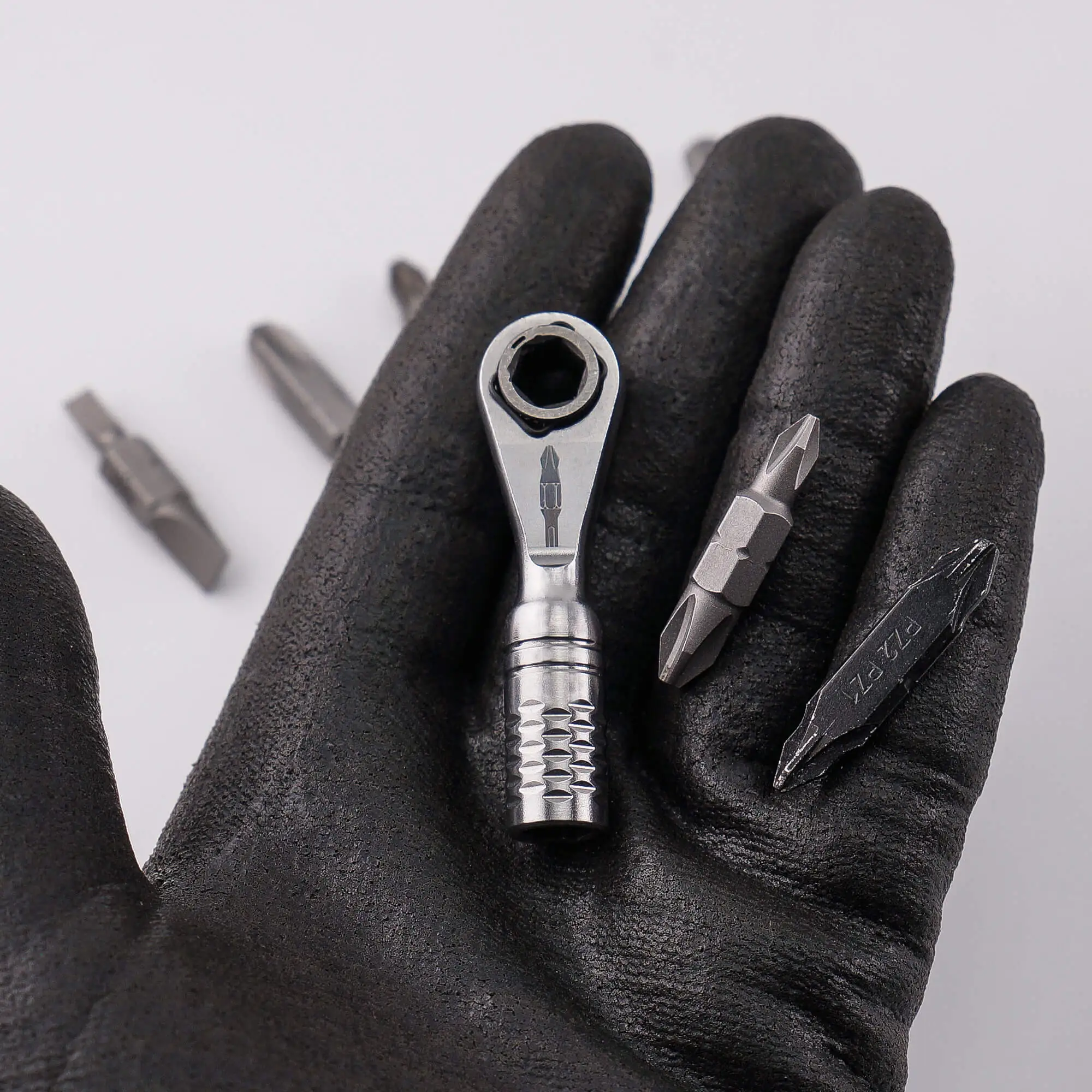 Gloved hand holding the 711L Mini Ratchet Wrench TG with double-ended bits in the background