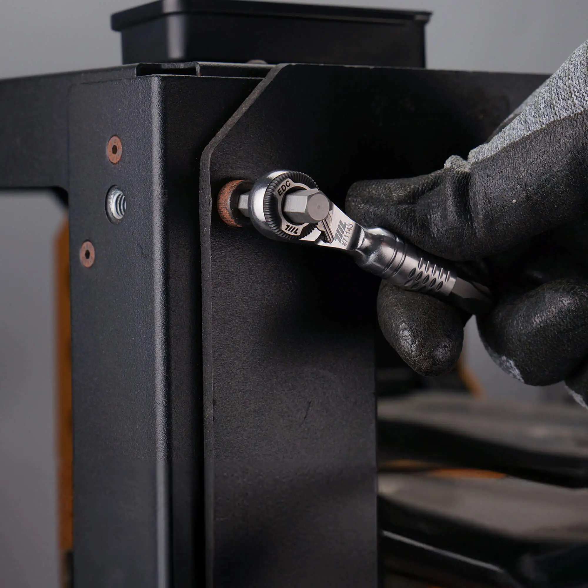 Mini ratchet wrench tightening a bolt on a black metal frame with a gloved hand